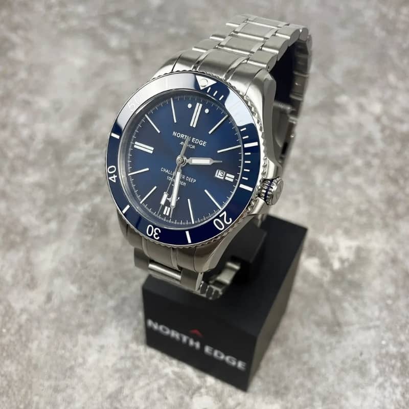 Silver watch with blue dial on a stand, branded 'North Edge', against a gray background.
